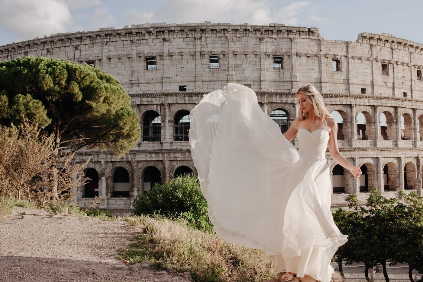 A couple in front of the Colosseum, her dress caught by the wind