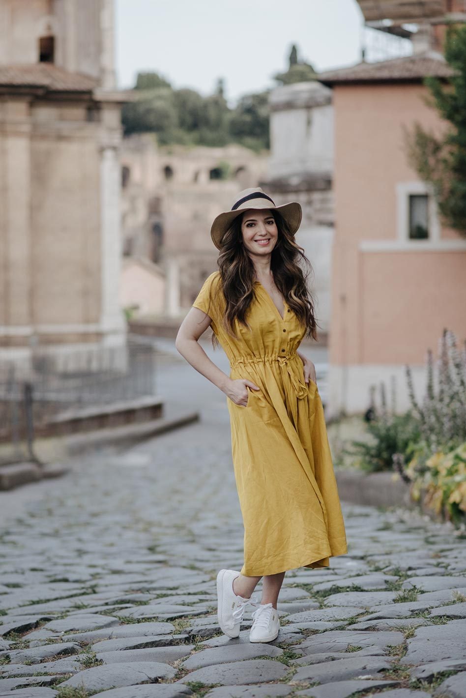 A woman in a yellow dress and straw hat on a cobbled street