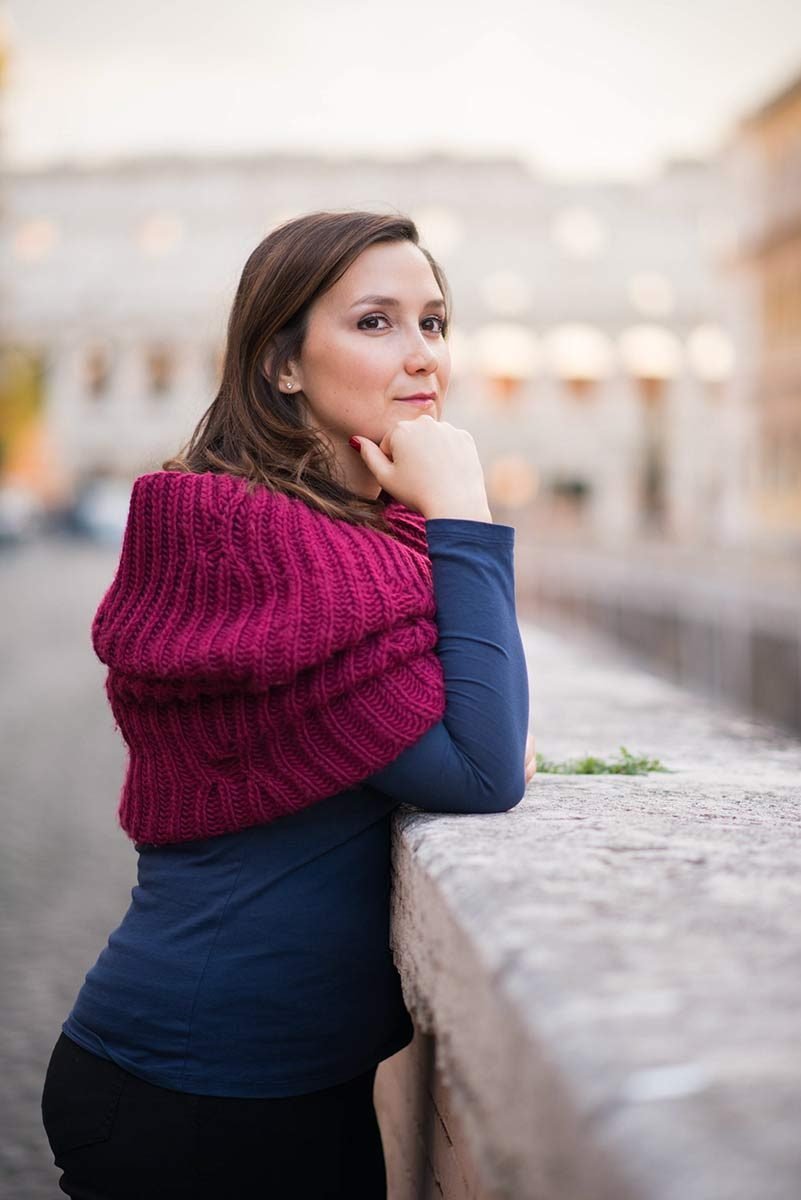 A woman in a red scarf leaning on a stone wall
